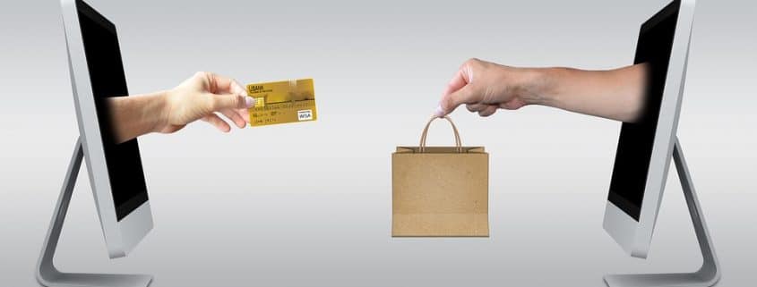 Graphic showing two desktops facing each other - one with a hand reaching out of it holding a bag, the other with a hand reaching out of it holding a credit card.