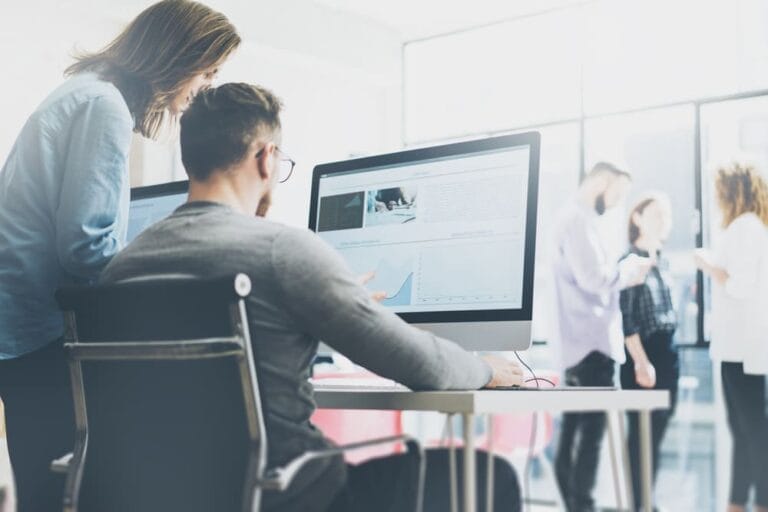 3 people talking in the background while a man and woman discuss what is on a computer screen.