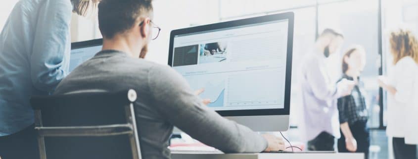 3 people talking in the background while a man and woman discuss what is on a computer screen.