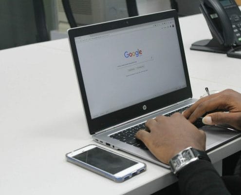 A man with a smartphone typing on a laptop in Google Search.