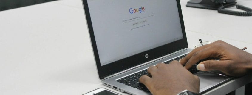 A man with a smartphone typing on a laptop in Google Search.