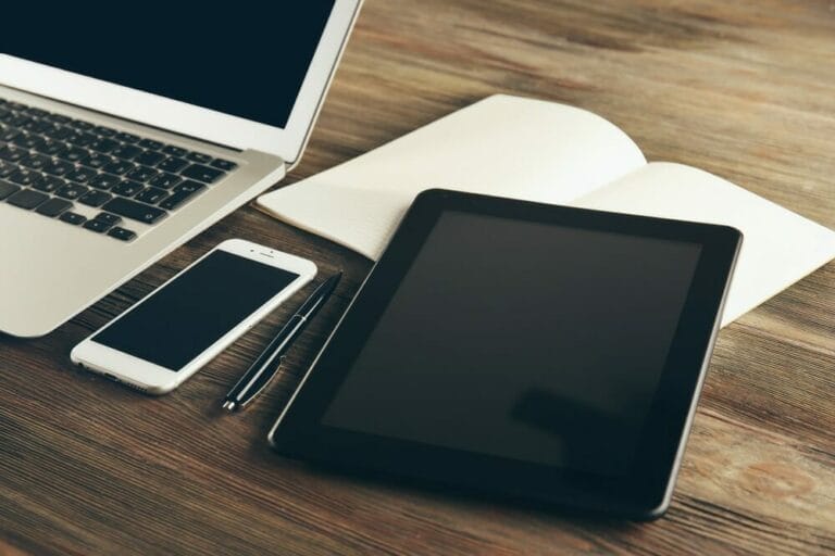 Desk with laptop, cell phone, tablet and notepad and pen