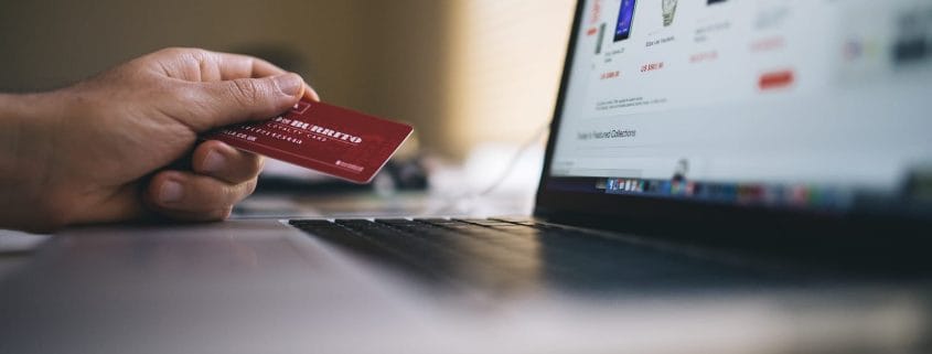 Male hand holding a credit card with a shopping site displayed on a laptop