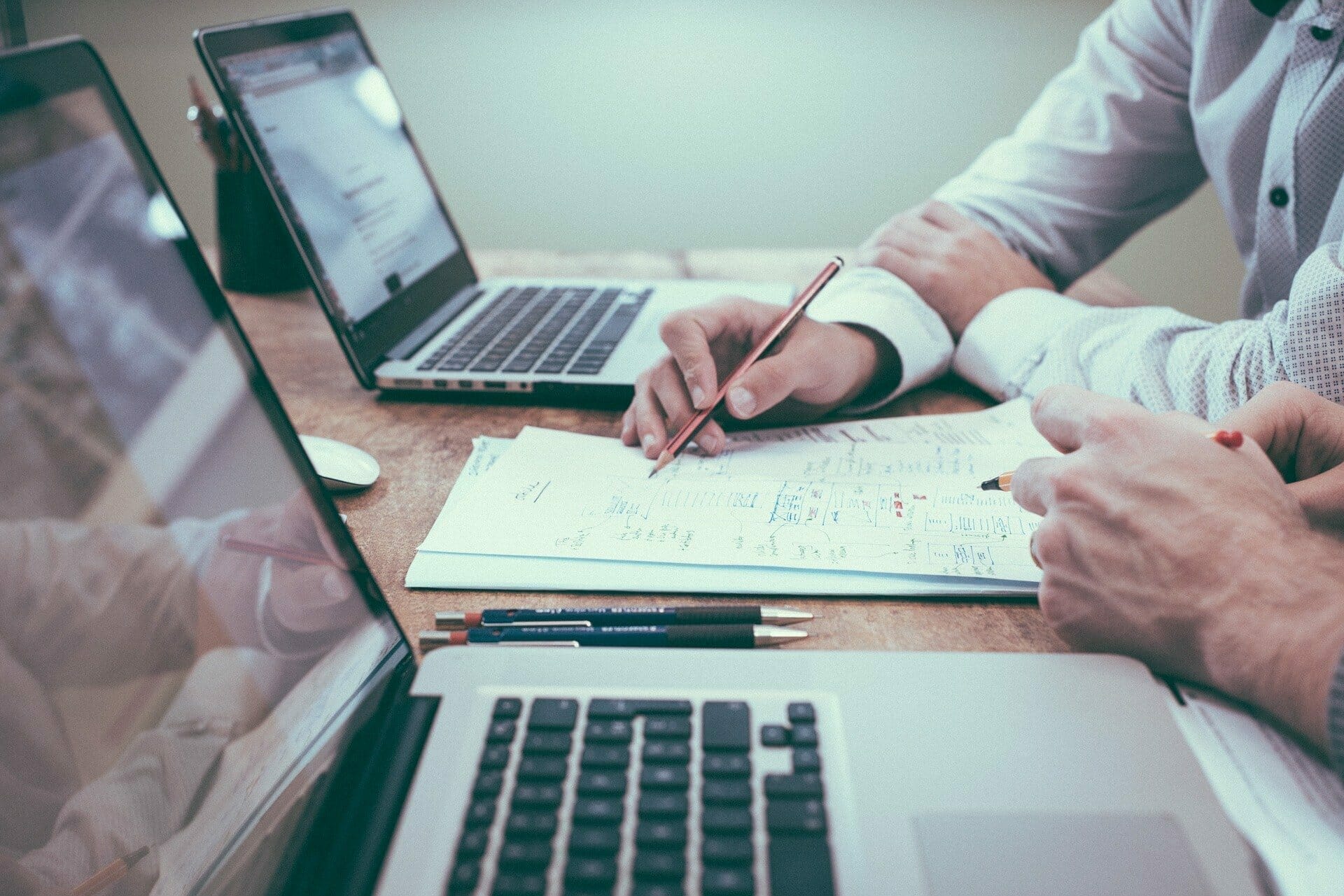 Two men at a table going over paperwork with 2 laptops nearby