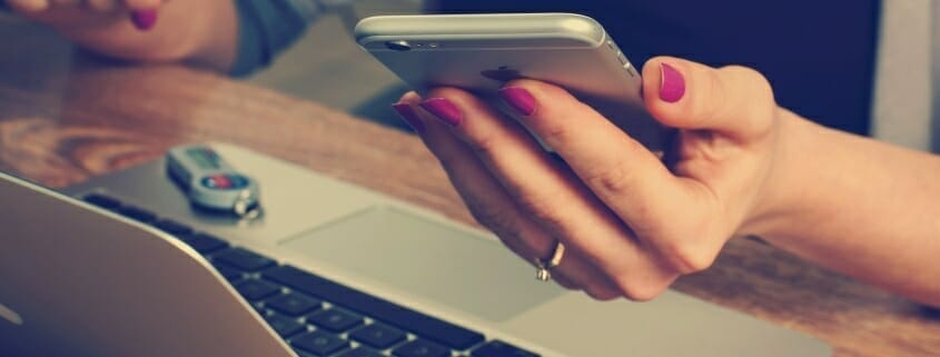 Female holding an iPhone with Laptop and flash drive next to her