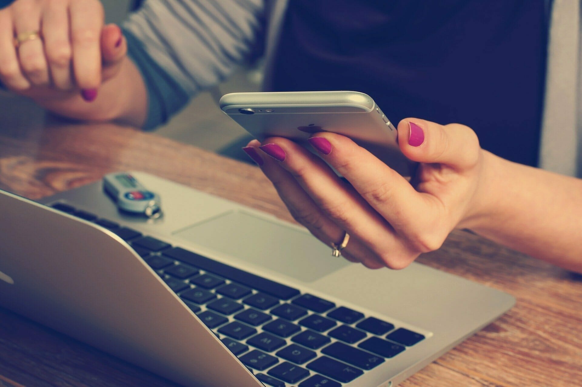 Female holding an iPhone with Laptop and flash drive next to her