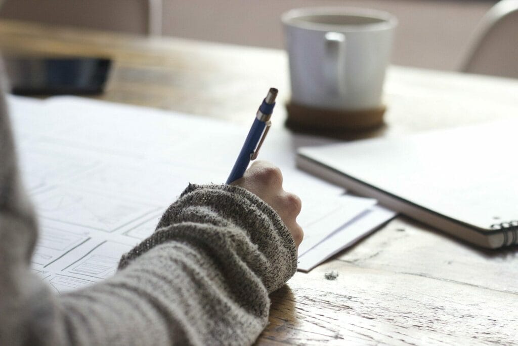 Female at a desk writing with a pen with coffee and notepad beside her