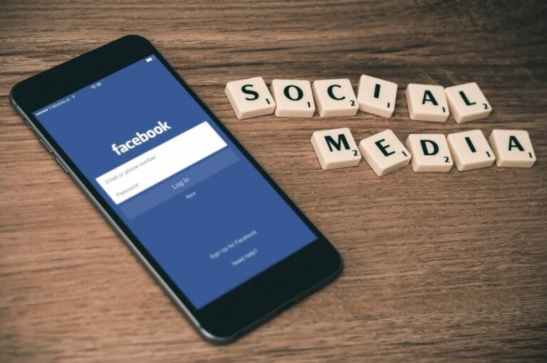 Cell phone showing Facebook Login page next to "Social Media" spelled out using Scrabble pieces