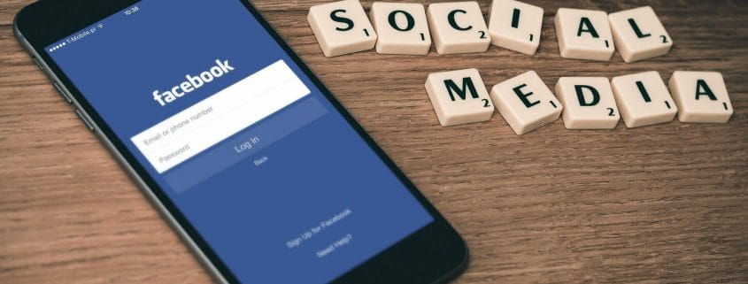Cell phone showing Facebook Login page next to "Social Media" spelled out using Scrabble pieces