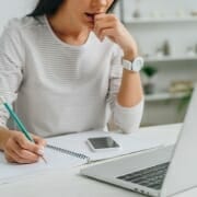 Woman with pad and pencil focused on laptop screen.