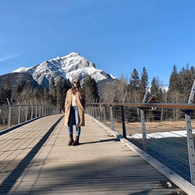 Young woman on a bridge with snow-capped mountains behind her.