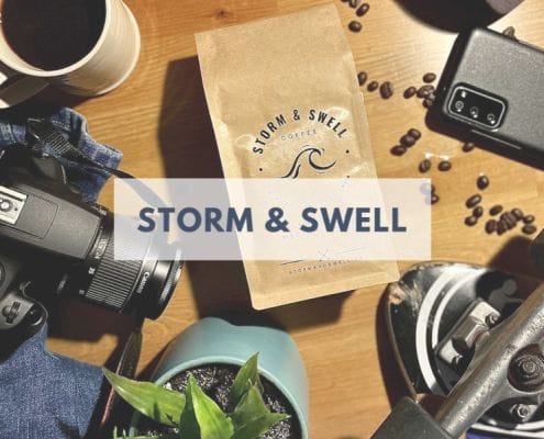 Storm & Swell brand name over an image of a bag of their coffee surrounded by a camera, smartphone, coffee, etc.