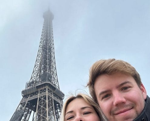 A young couple in a selfie with the Eiffel Tower in the background.