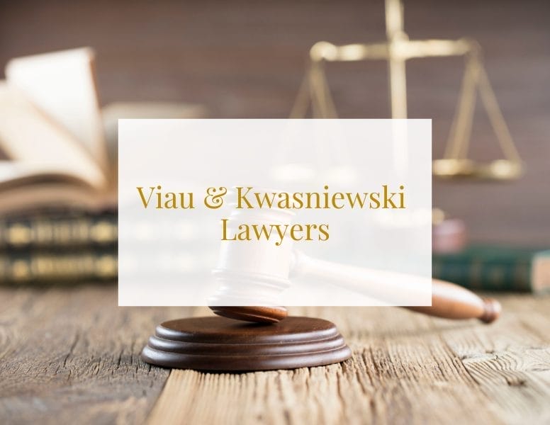 A gavel rests on a wooden table with an out-of-focus balance scale and open books in the background. Overlaid text reads "Viau & Kwasniewski Lawyers.