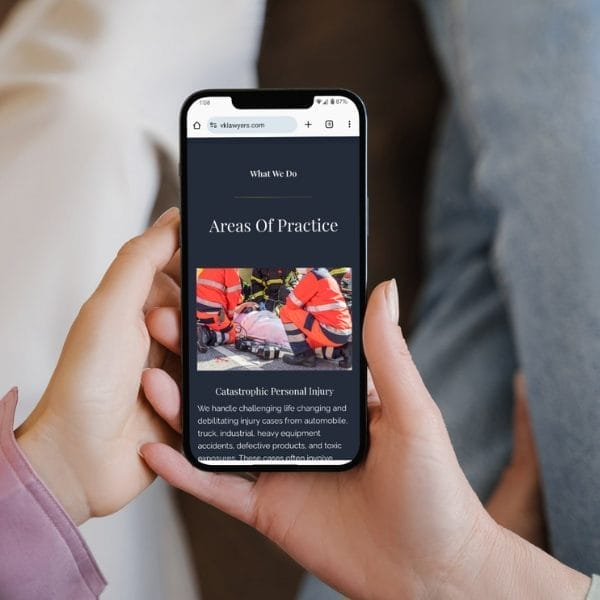 A person is holding a smartphone displaying a webpage titled "Areas Of Practice" with a section on "Catastrophic Personal Injury." The image on the screen shows rescue workers in orange vests attending to an emergency scene.