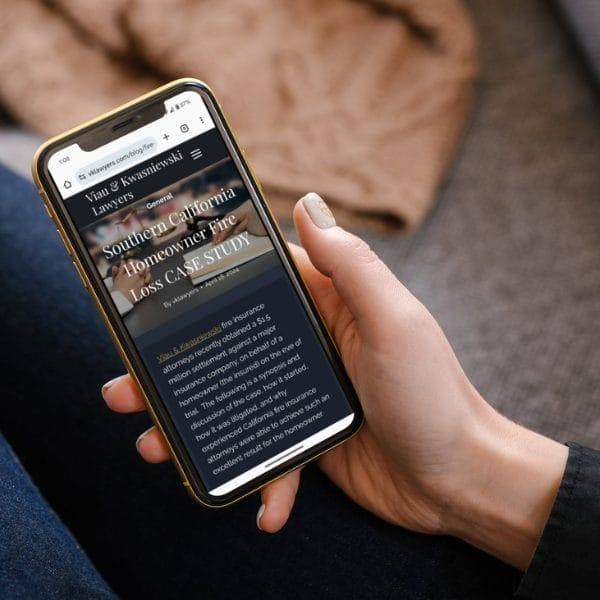 A person holding a smartphone showing a legal case study about a Southern California homeowner fire loss by Viau & Kwasniewski Lawyers. The screen displays text from the firm's website.