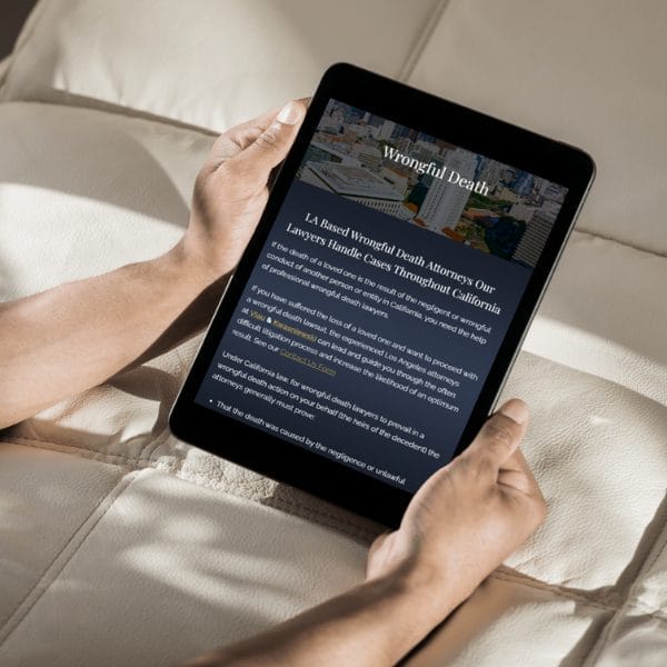 Person holding a tablet displaying information about wrongful death attorneys, mentioning services in California. The tablet screen shows text on a dark background with a section of an image at the top, resting on a light-colored surface.