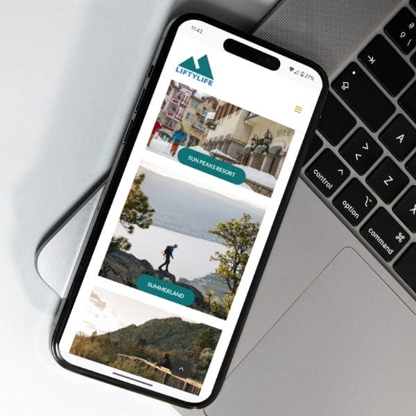 A smartphone displaying a travel-themed website with images of scenic locations, including mountains and a reservoir. The phone is placed on a laptop keyboard. The website's logo says "LiftyLife" at the top.