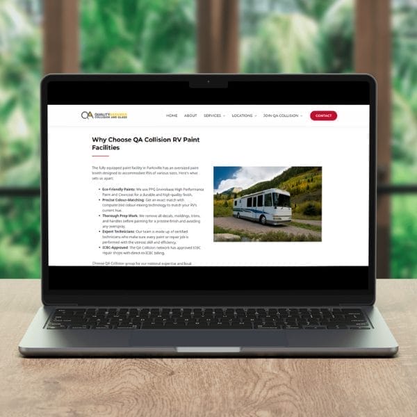 A laptop displaying a webpage about QA Collision RV Paint Facilities. The screen shows text and an image of a white RV on a scenic road. The background is out of focus, featuring lush green foliage.