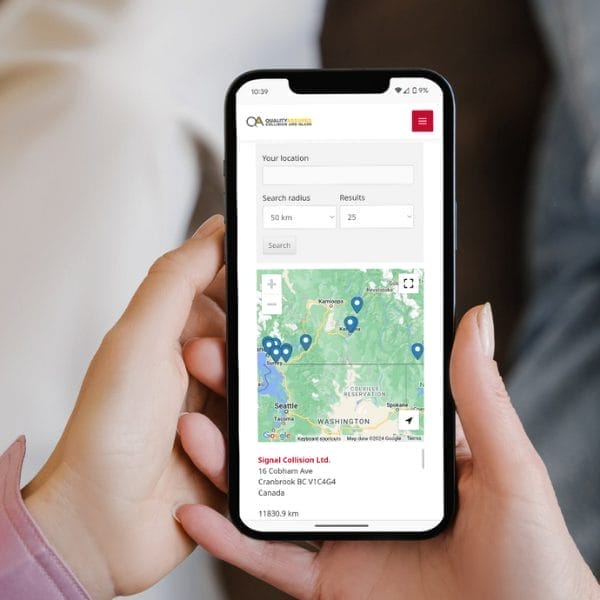 A person holding a smartphone displaying a map of Washington state and nearby areas. The screen shows blue location markers and search options. The phone is held with both hands, and the background is blurred.
