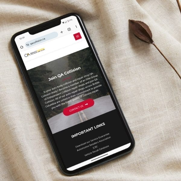 Smartphone on a fabric surface displaying a website for "QA Collision" with options like "Contact Us" and "Important Links." A small decorative leaf is placed nearby.
