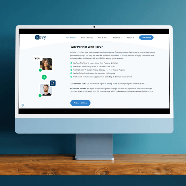 A computer monitor displays a website with the title "Why Partner With Revy?" featuring text and icons. The background is a blue-green gradient wall, and the monitor is on a wooden surface.