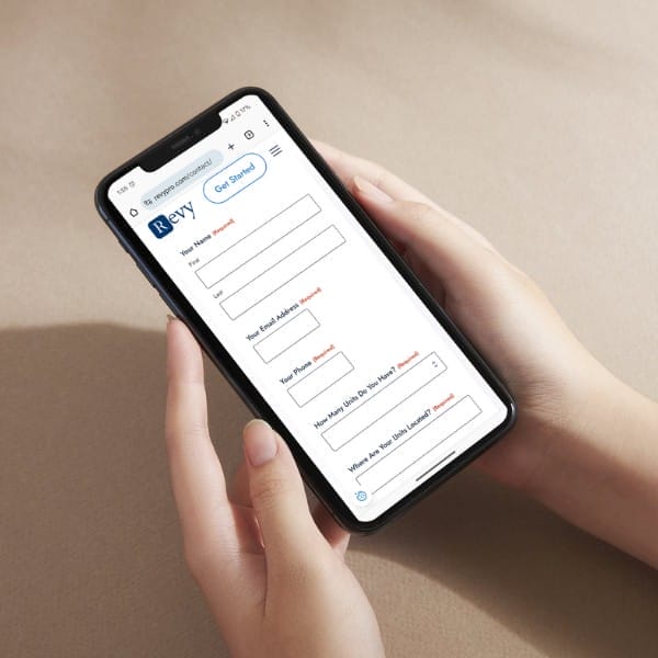 A person holding a smartphone displaying a form on the screen. The form includes fields for a name, email address, phone number, and question about joining an event. The phone has a black case and the background is a neutral color.