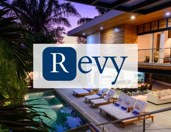 Modern outdoor lounge area at dusk with a swimming pool, surrounded by lush greenery. Sun loungers line the poolside, and a spacious open-air room with large windows is visible. The Revy logo is prominently displayed in the center.