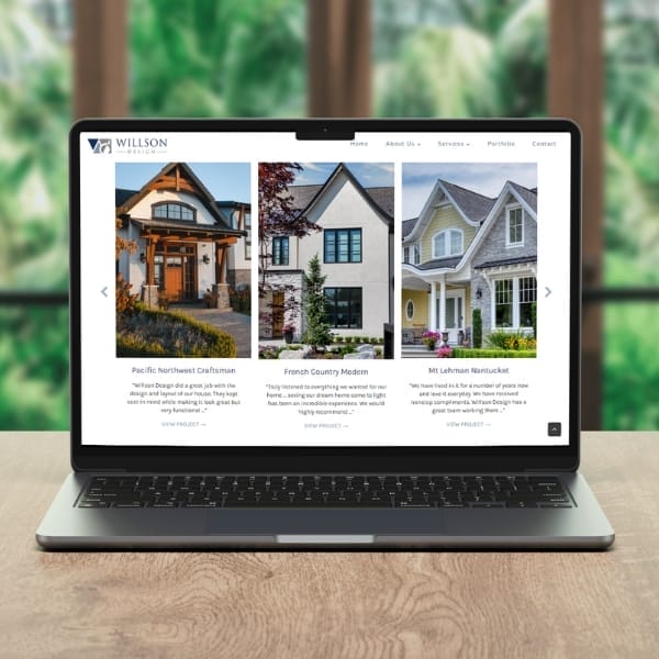 A laptop on a wooden table displays a website with images of three homes and descriptions: Pacific Northwest Craftsman, French Country Modern, and Mt. Lehman Nantucket. The website header includes links to Home, About Us, Services, and Portfolio.
