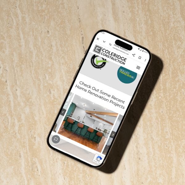 Smartphone displaying a construction company's website. The screen shows an image of a modern kitchen with green chairs and a wooden floor. The site name "Coleridge Construction" is visible at the top. The phone is on a beige marble surface.