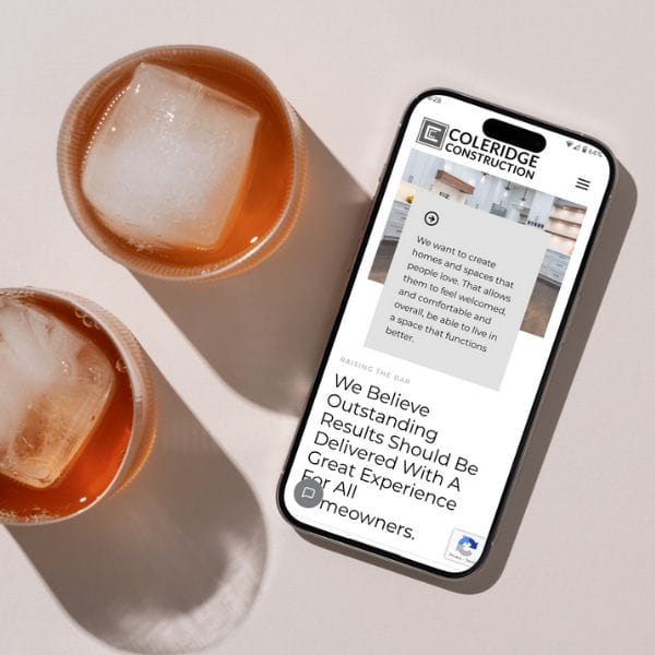 A smartphone displaying the Cole Ridge Construction website is placed on a light-colored surface next to two iced coffee glasses. The website shows text about creating homes with outstanding results.