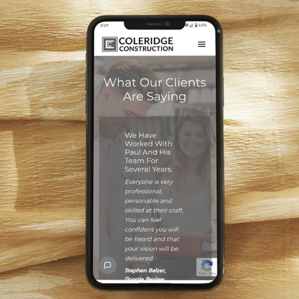 A smartphone displaying a website for Coleridge Construction rests on a wooden surface. The screen shows a client testimonial praising Paul and his team for their professionalism and skill.
