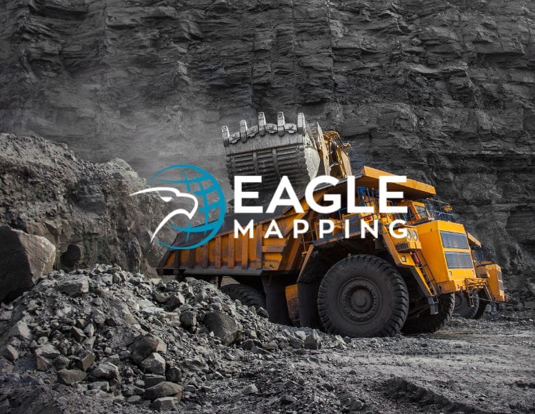 A large yellow mining truck is being loaded with rocks in a quarry. The background features rugged gray rock walls. Overlaid on the image is the "Eagle Mapping" logo, featuring a stylized eagle head.