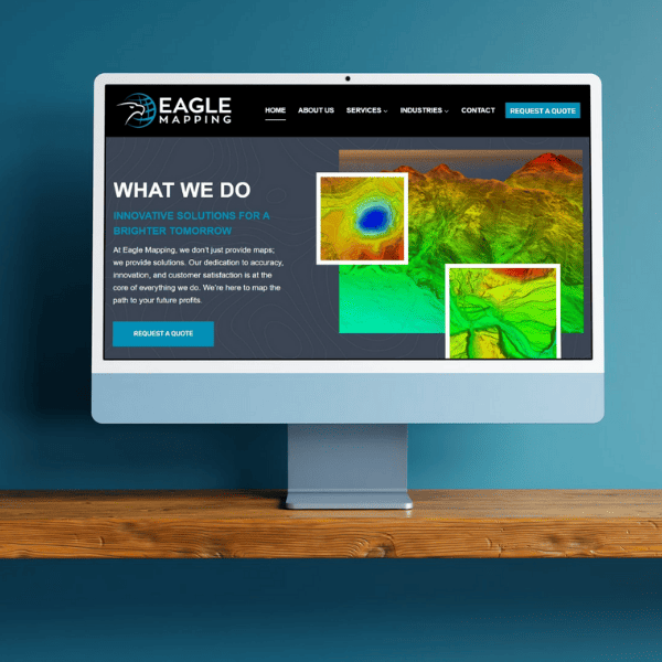 A computer monitor displaying a webpage for "Eagle Mapping." The page features vibrant topographic maps and text about the company's mapping solutions. A "Request a Quote" button is present. The monitor is on a wooden surface against a blue background.