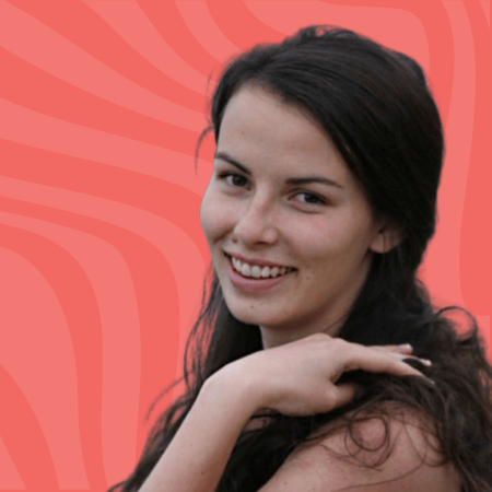 Smiling person with long dark hair against a wavy coral background, resting their chin on their hand.