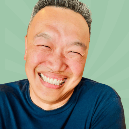 A person with short hair is smiling broadly against a green, radial background. They are wearing a dark T-shirt.