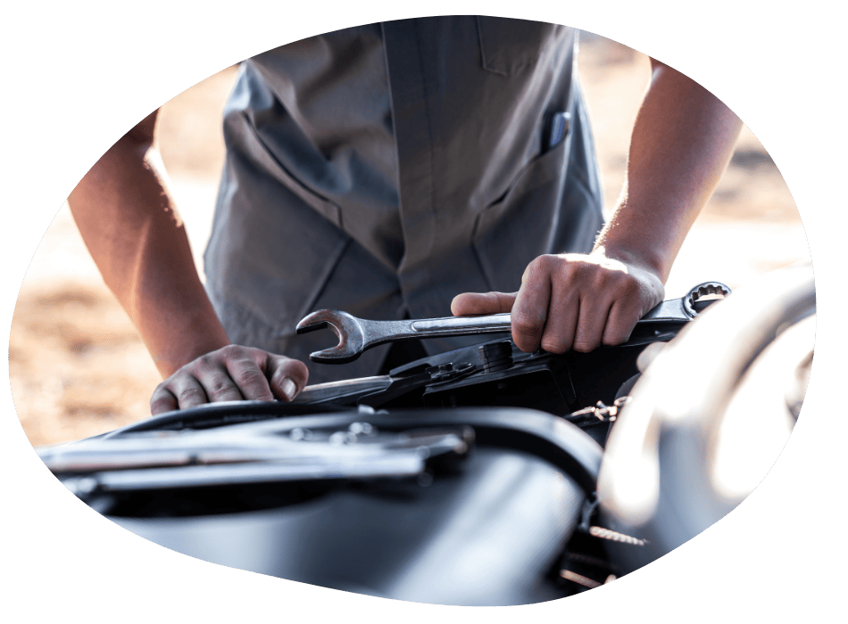 Person in a grey shirt holding a wrench while working on a vehicle engine.