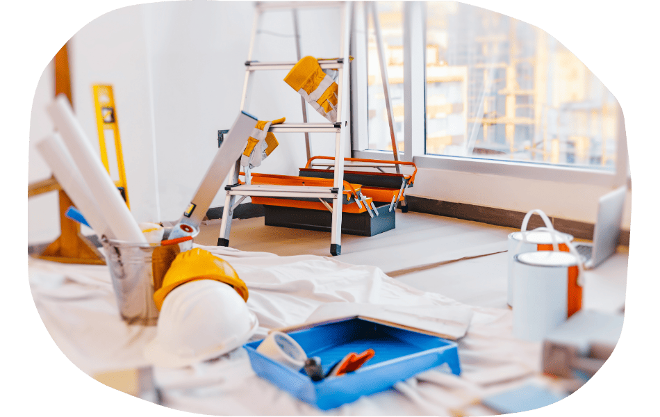 A room under renovation with a ladder, paint cans, a hard hat, tools, and industry specific web design plans scattered on a floor covered by a drop cloth near large windows.