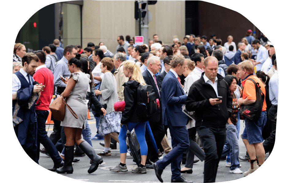 A large crowd of people walk in different directions at a busy city crosswalk, many looking at their phones or talking—reflecting the need for industry specific web design that caters to both business and casual users on the go.