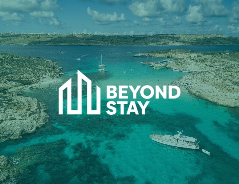 A turquoise bay with boats anchored in clear water, green hills in the background, and the white "BEYOND STAY" logo with stylized building shapes at the center, reflecting the modern touch found in GLC Equipment website design.